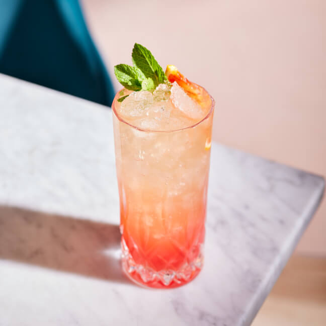 A tall glass of an English Garden mocktail with crushed ice, mint sprig, and grapefruit slice garnish.